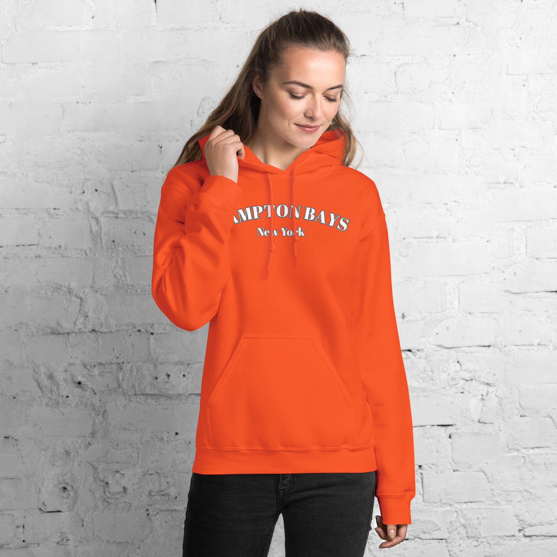 Bright orange Hampton Bays Hoodie modeled indoors, soft cotton unisex sweatshirt perfect for beach lovers and fall layering.